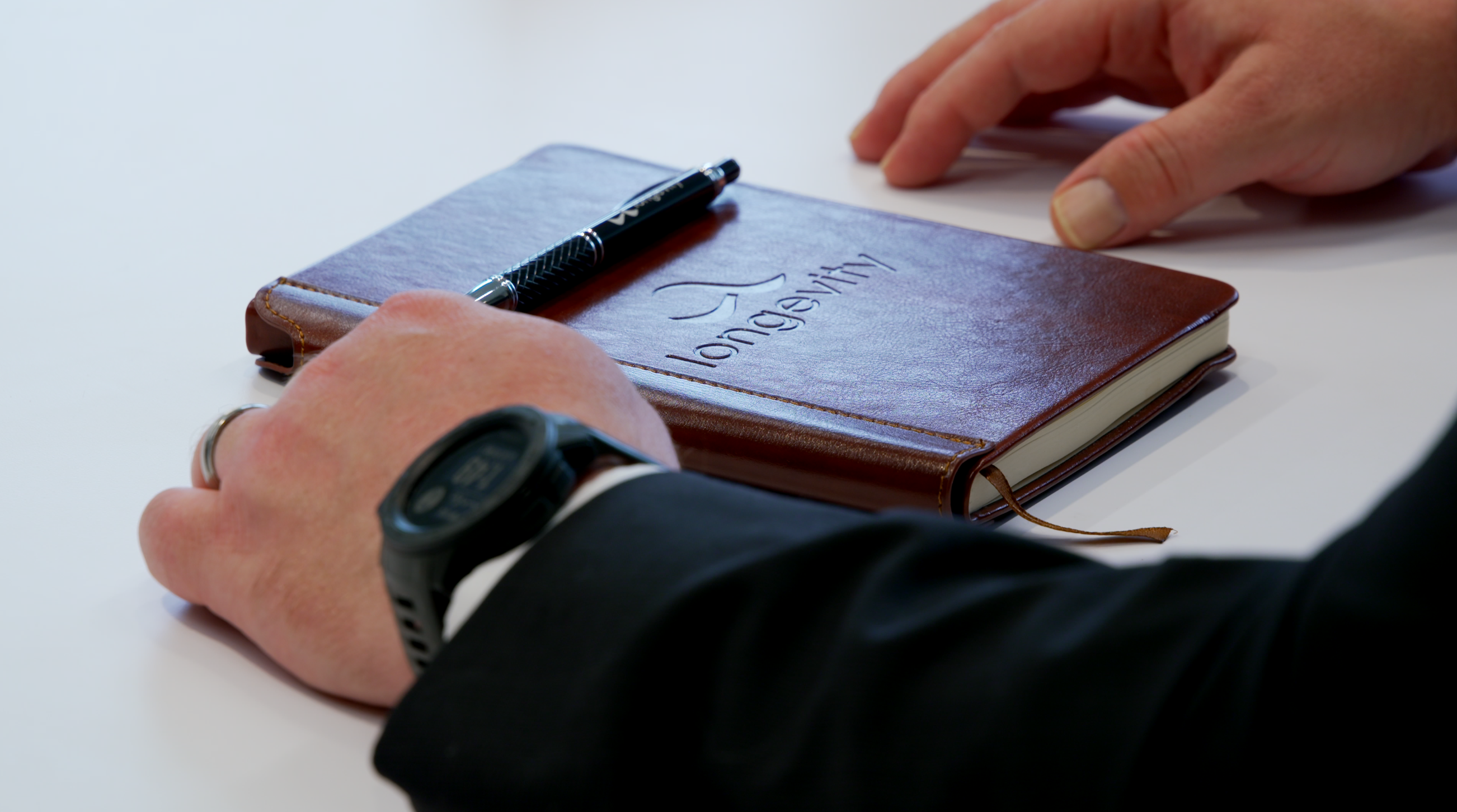 Notebook with the longevity name on the cover sitting on a table. Pen resting on top.